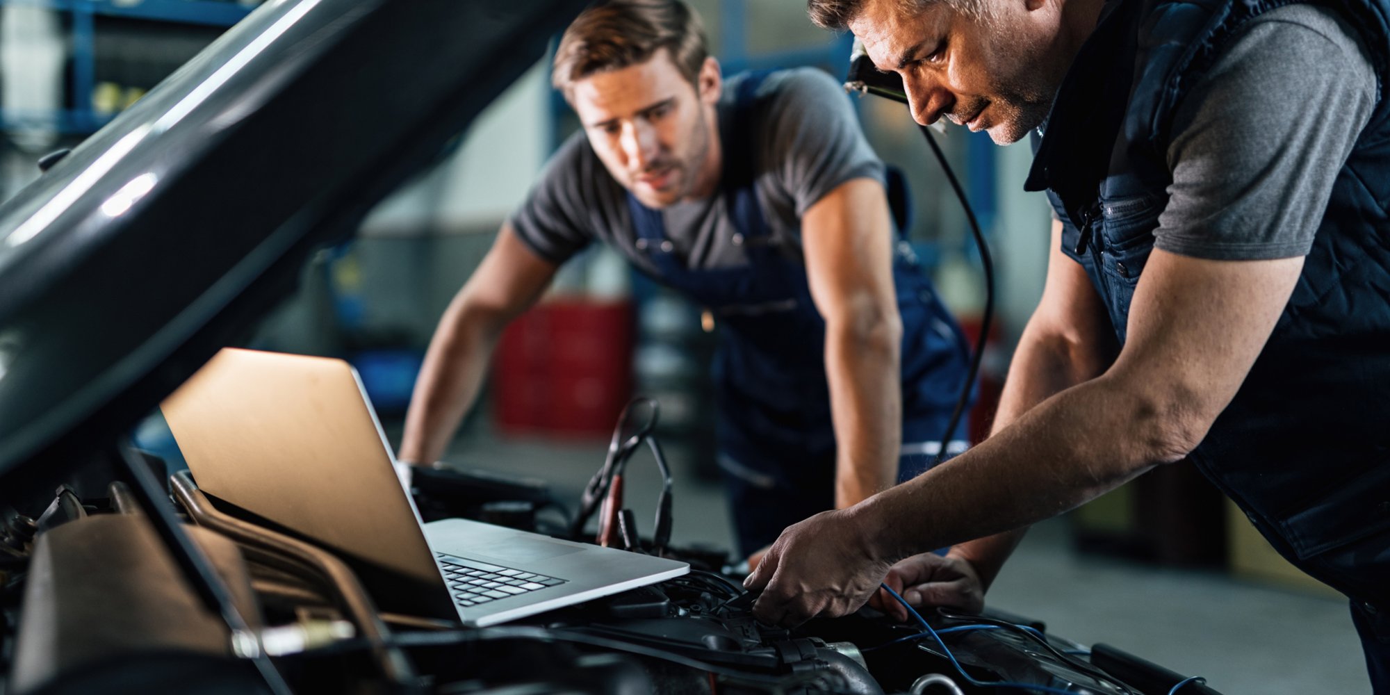 Zwei Mechaniker arbeiten konzentriert an einem Auto und nutzen dabei einen Laptop zur Diagnose.