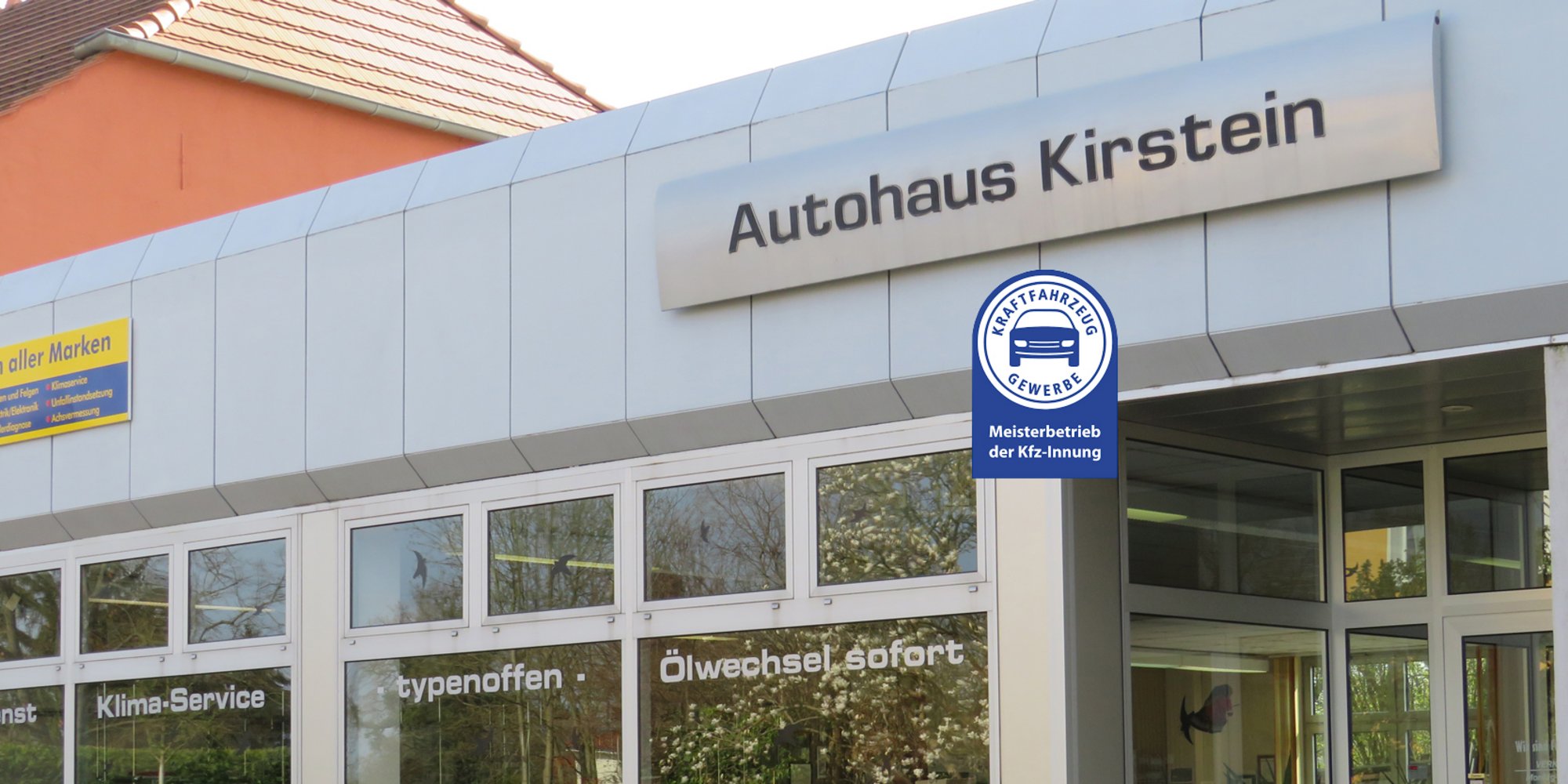 Die Fassade eines Autohauses mit der Aufschrift „Autohaus Kirstein“ und Schildern, die Kfz-Services bewerben.